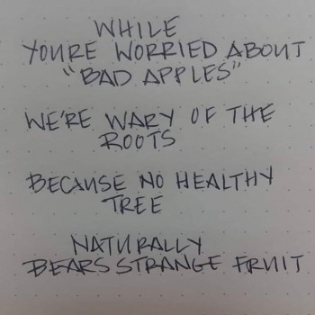 Poem handwritten with black ink on grid paper. Poem reads: While you're worried about "bad apples" / We're wary of the roots / Because no healthy tree / Naturally bears strange fruit