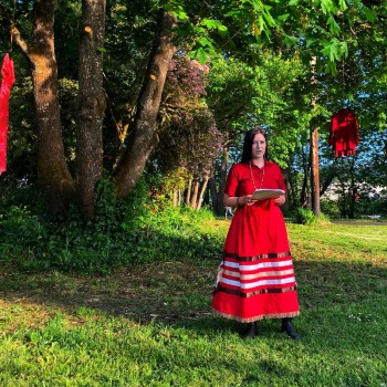 University of Oregon student and Indigenous activist Violet Johnson reads a poem under one of several trees adorned with red dresses Wednesday night. CREDIT BRIAN BULL / KLCC