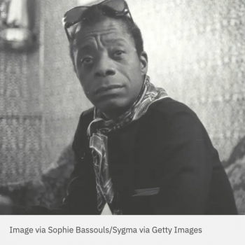 Black and white photo of James Baldwin seated wearing a black jacket, scarf, and sunglasses on his head. Caption below reads "Image via Sophie Bassouls/Sygma via Getty Images"