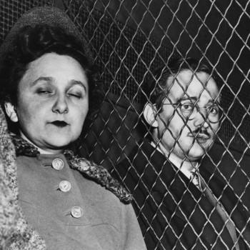 black & white image of Ethel & Julius seated at Sing Sing, they are separated by a chain link fence, facing the camera. 