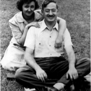 Black and white photo of Ethel & Julius Rosenberg posing for a photo in the park. Both are seated, Ethel's arms are around Julius.