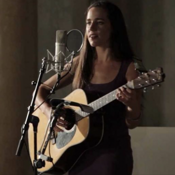 Photo of activist artist Jean Rohe with her guitar at the microphone in performance.