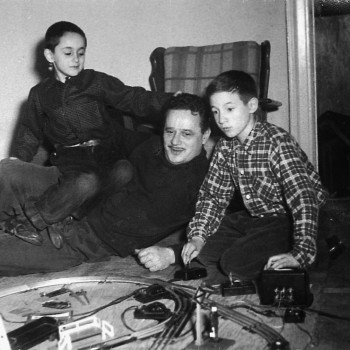 a black and white photo, Abel Meeropol with his sons Robert and Michael as young children playing with a model train set on the floor.