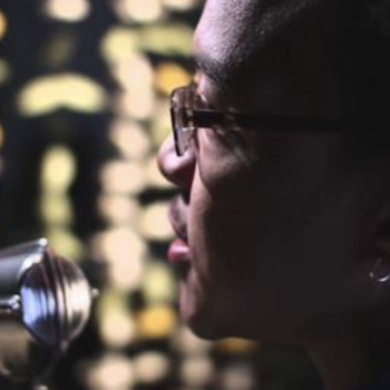 Still-frame from the "Strange Fruit" video by the SALT Project. A close up of one of the narrators at the microphone.