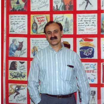 Robert Meeropol from the early days of the RFC about 30 years ago. He poses in front of a large quilt (red with white boxes filled with pictures, quotes & designs)