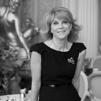 black and white photo of Anne Sebba, smiling and posing in a highly decorated dining room